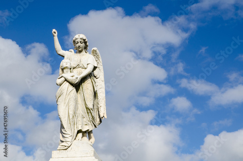 Angel statue standing against clouds blue sky.