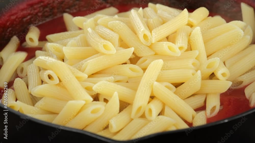 Putting pasta penne in pan with tomato sauce in pan, close up. Cooking traditional Italian dinner. 4K UHD video Putting pasta penne in pan with tomato sauce in pan, close up. Cooking traditional Italian dinner. 4K UHD video