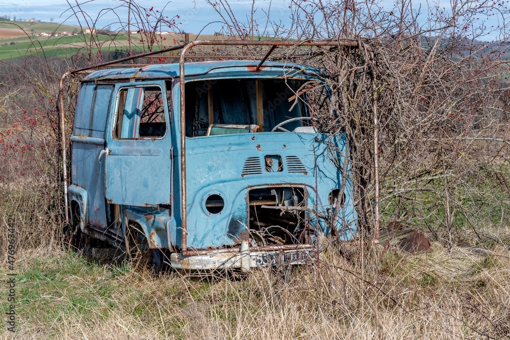 Vieux véhicule bleu abandonné en pleine campagne et recouvert de ronces