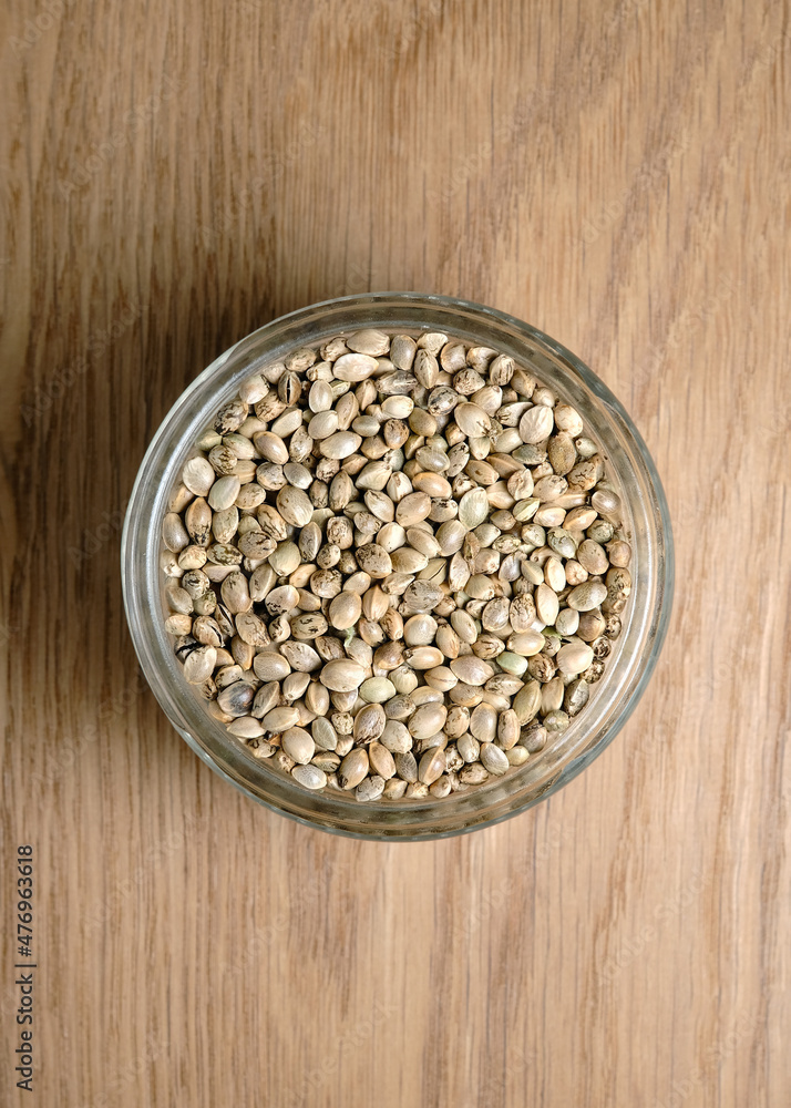 Hemp seeds, edible cannabis production. Marijuana grain in a round glass bowl on wooden texture background. Hemp seeds, edible cannabis production. Marijuana grain in a round glass bowl on wooden texture background.