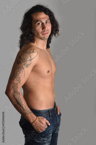 portrait of a man with tattoos and long hair looking at camera on gray background