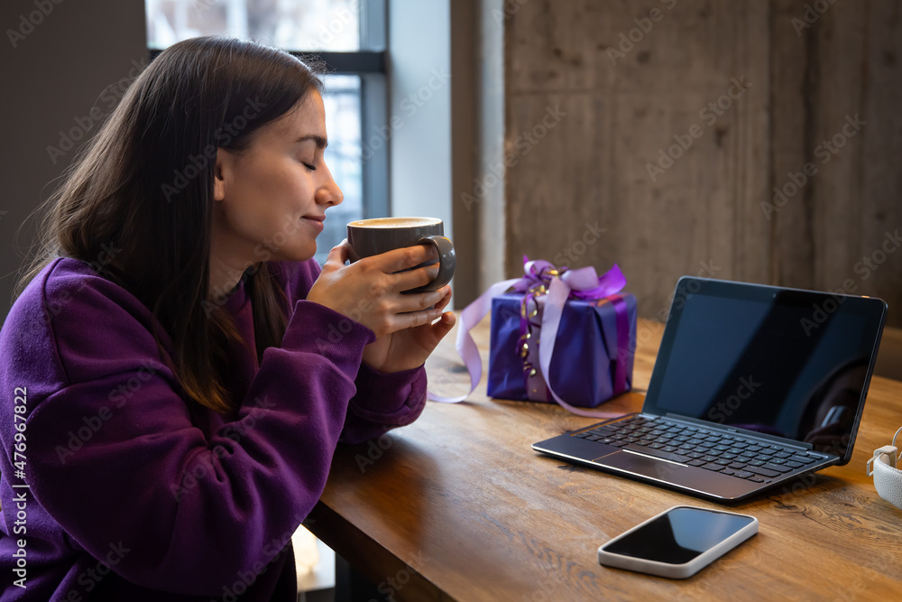 Young woman with coffee and gift box in front of laptop. Young woman with coffee and gift box in front of laptop.
