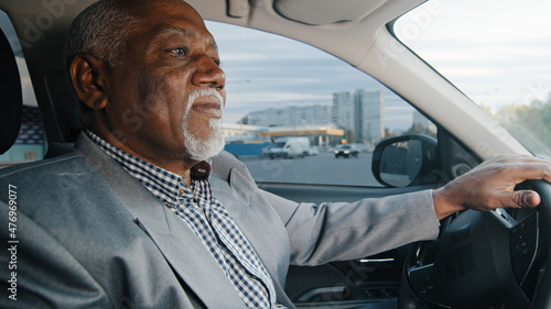 Old african american man driving car serious pensive elderly male leaves parking lot mature businessman looking closely at road drives up approaches intersection experienced driver ride on highway