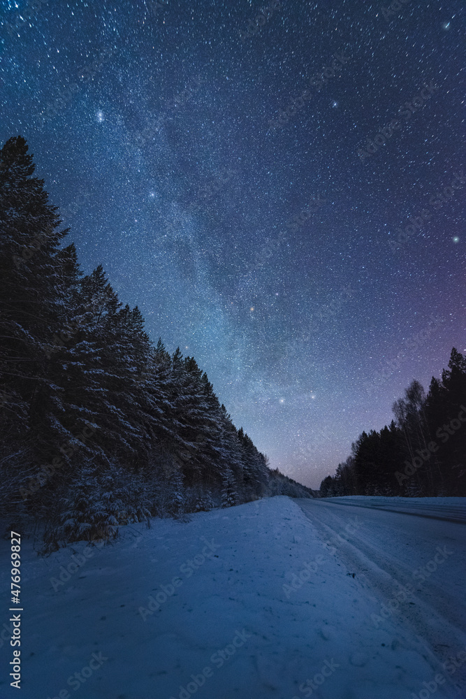Winter road in the forest under beautiful night sky with Milky Way and ...