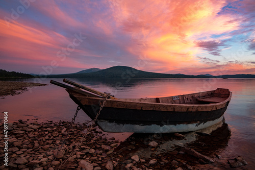 Boat moored by the lake, under a magnificent sunset sky with orange and pink clouds