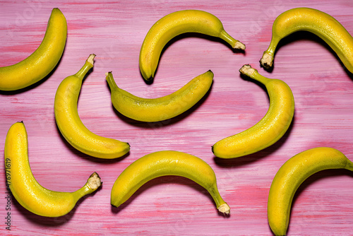 Varios plátanos en distintas posiciones vistos desde arriba sobre mesa de color fucsia