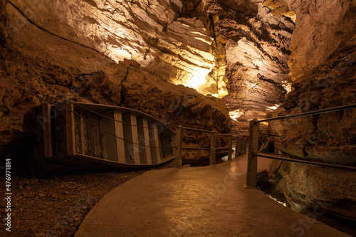 Entrance to an old brown cave illuminated by yellow lights and a small old boat on its side