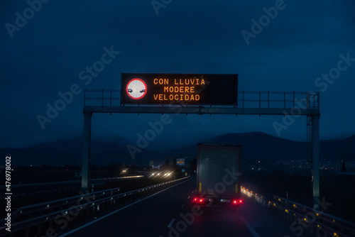 Illuminated panel of a highway on a rainy night with the legend "in rain, moderate speed"