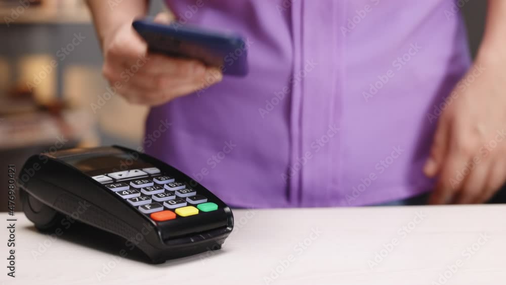 Closeup of female hands with pos-terminal of employee and cellphone. Pay by phone on electronic payment machine or card reader. E-money at cashless wallet. Client buys food order at coffee place. Closeup of female hands with pos-terminal of employee and cellphone. Pay by phone on electronic payment machine or card reader. E-money at cashless wallet. Client buys food order at coffee place.