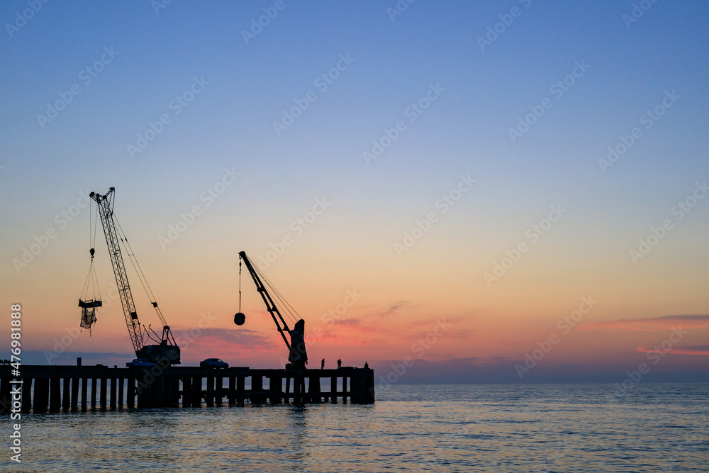 sunset at sea, evening at sea. against the background of a beautiful sky, a silhouette of a pier with lifting mechanisms