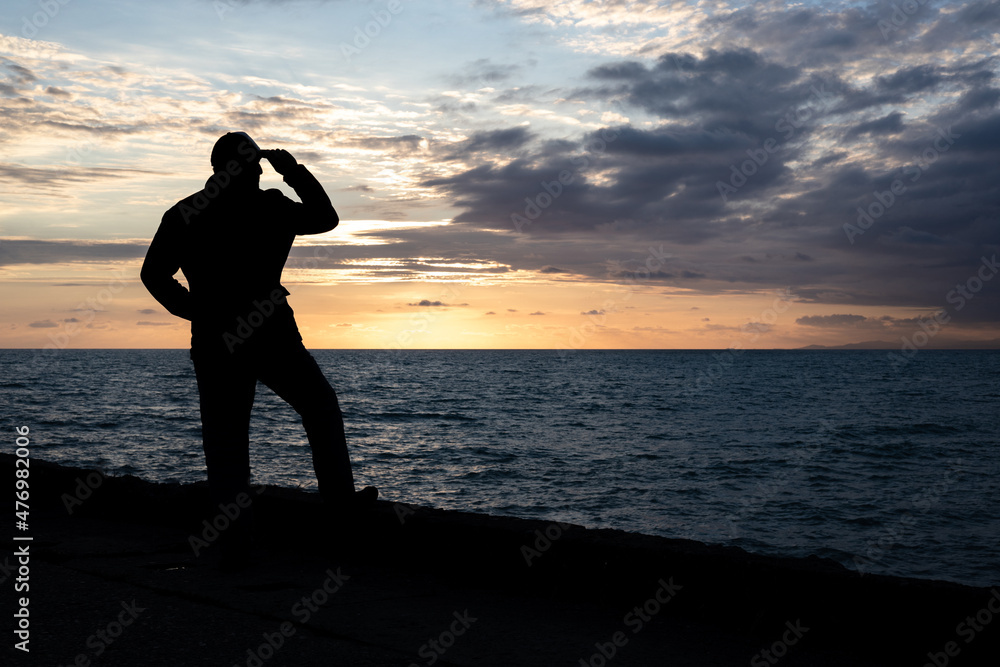 silhouette of a man standing on the pier and looking at the sea during sunset