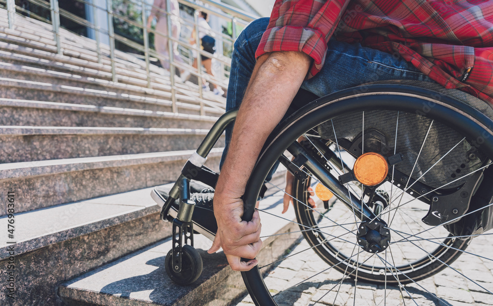 Naklejka premium Young man with a physical disability who uses wheelchair in front of the stairs