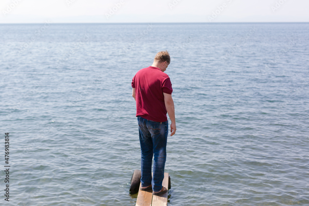 A tall adult man on a narrow wooden bridge river is calling for help.