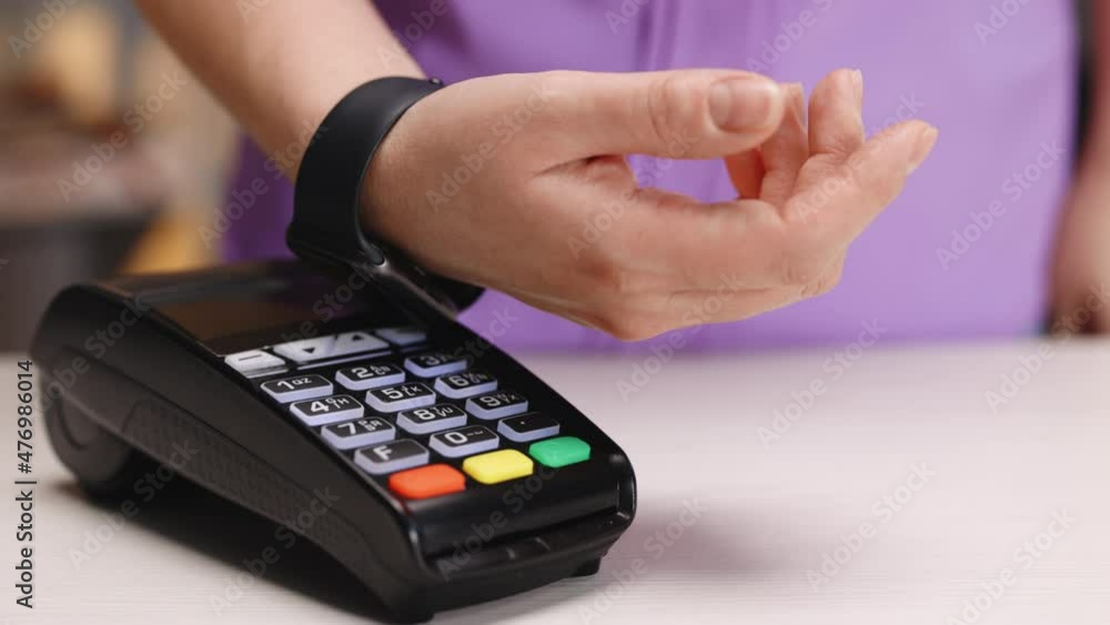 Pay by smart watch on electronic payment machine or card reader. E-money at cashless wallet. Female client hand on pos-terminal of seller or store employee at coffee place or food supermarket Pay by smart watch on electronic payment machine or card reader. E-money at cashless wallet. Female client hand on pos-terminal of seller or store employee at coffee place or food supermarket