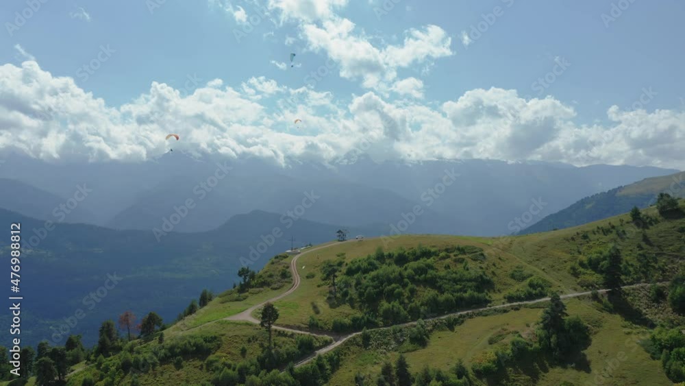 Paragliding on a background of clouds on a sunny summer day. Aerial view of athletes flying on parachutes against the backdrop of a mountain landscape and a horizon covered with clouds. Paragliding on a background of clouds on a sunny summer day. Aerial view of athletes flying on parachutes against the backdrop of a mountain landscape and a horizon covered with clouds.