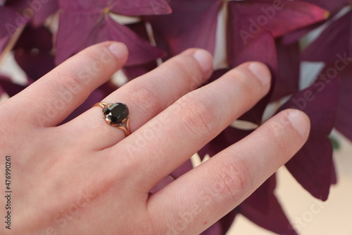 Old fashion ring with black stone on finger. purple plant in backround