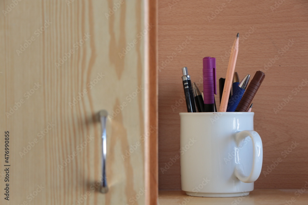 Obraz premium Pens in the white cup. Felt-tip pen,ball-point pen, lead pencil, waterproof marker. Wood in background.