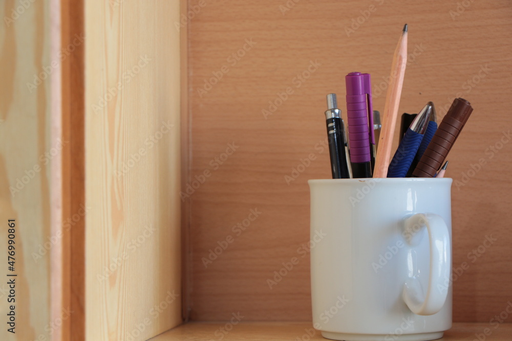 Pens in the white cup. Felt-tip pen,ball-point pen, lead pencil, waterproof marker. Wood in background. Pens in the white cup. Felt-tip pen,ball-point pen, lead pencil, waterproof marker. Wood in background.