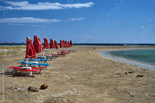 Umbrellas and beach beds on a windy day on the sandy coast of Crete island © GKor