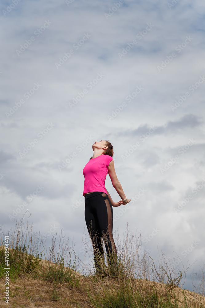Young sporty woman in sportswear on hill top stretching or warming up on cloudy sky background. Fitness, healthy way of life, wellbeing, freedom, loosing weight concept. Young sporty woman in sportswear on hill top stretching or warming up on cloudy sky background. Fitness, healthy way of life, wellbeing, freedom, loosing weight concept.
