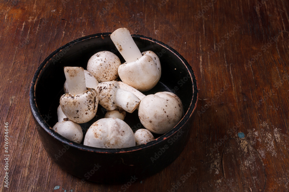 Wooden bowl of fresh raw champignon mushrooms on kitchen table. Autumn harvest, seasonal jrganic vegan food, healhty eating habits. Wooden bowl of fresh raw champignon mushrooms on kitchen table. Autumn harvest, seasonal jrganic vegan food, healhty eating habits.