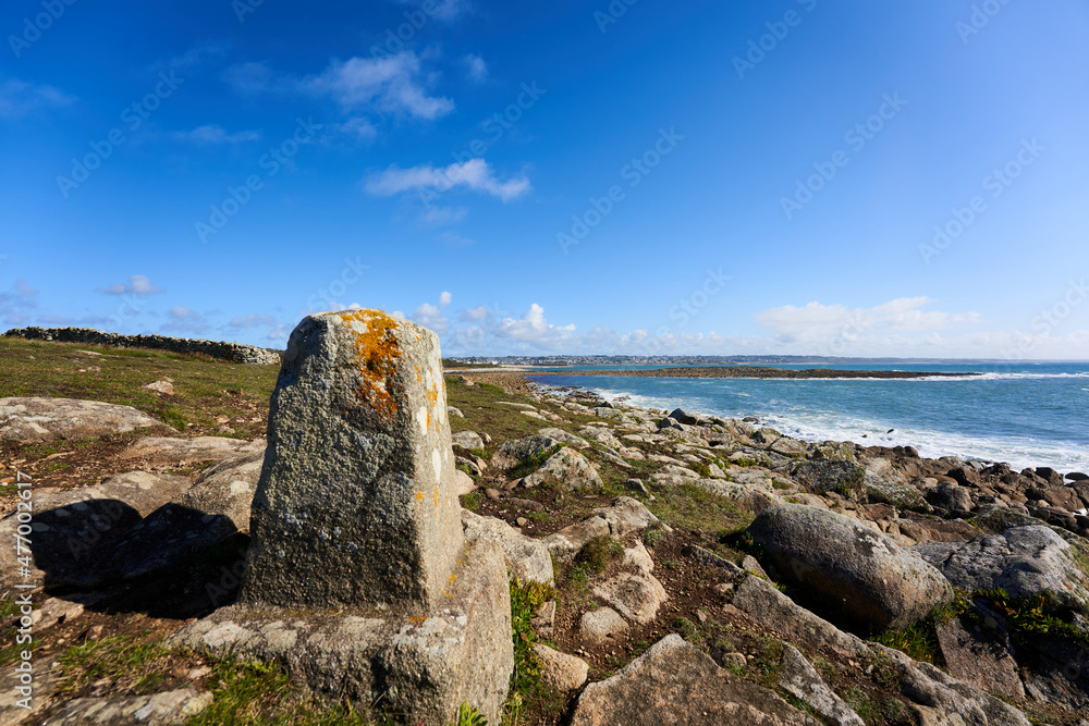 Boundary stone on the Breton coast. Landscape with sea water against blue sky. Rocky background. France, Brittany, Audierne, Lervily. Boundary stone on the Breton coast. Landscape with sea water against blue sky. Rocky background. France, Brittany, Audierne, Lervily.