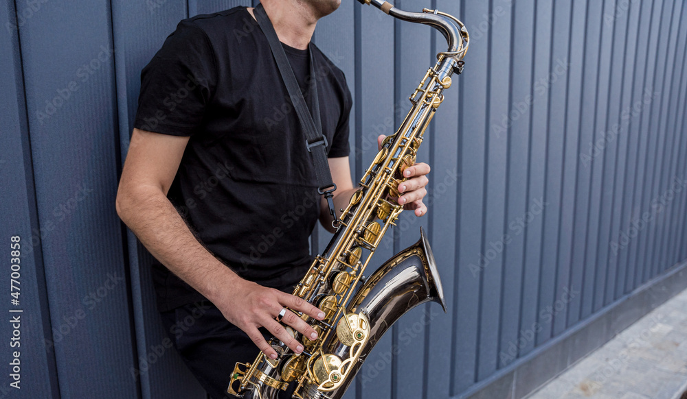 Fototapeta premium Young street musician playing saxophone near the big blue wall