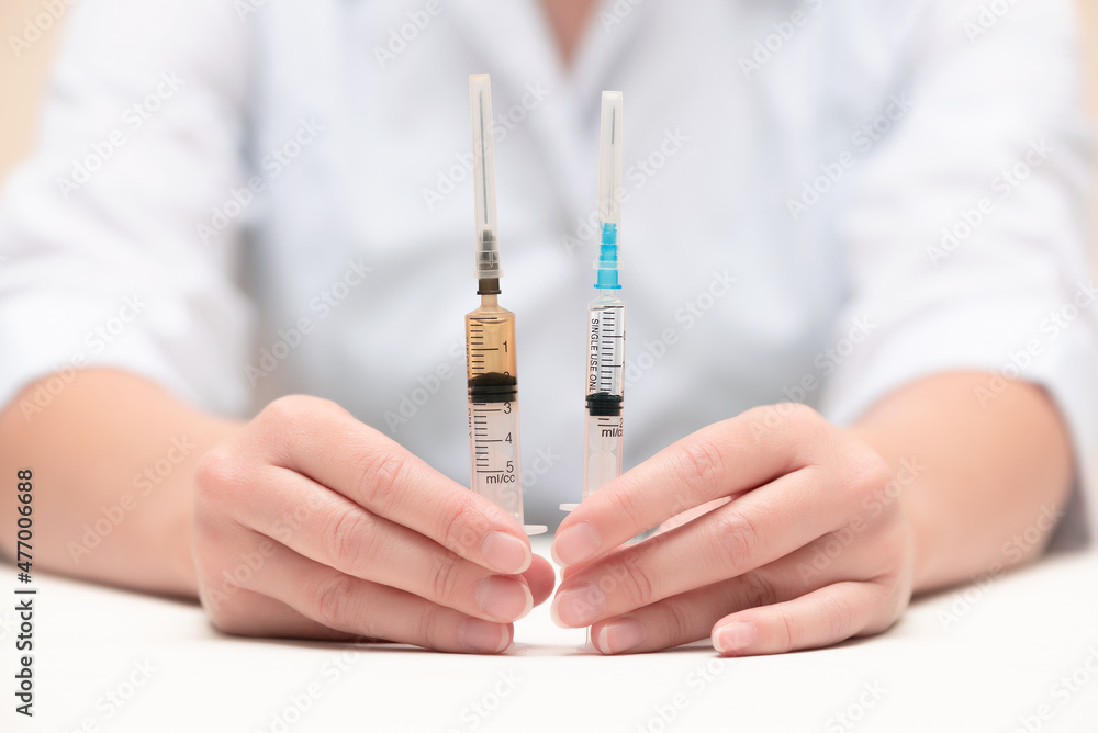 A doctor shows in hand a two various syringe with a liquid. Comparison of vaccine or anesthetic concept. A doctor shows in hand a two various syringe with a liquid. Comparison of vaccine or anesthetic concept.