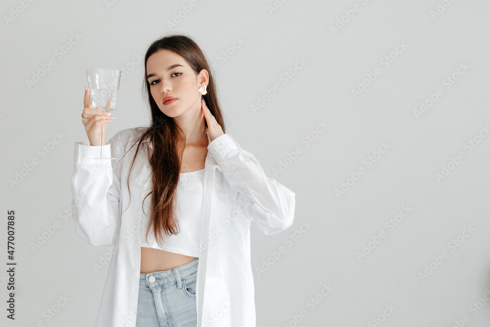 Young serious woman cares about her health, holding glass of water looking at the camera, studio portrait on white. Morning routine concept Young serious woman cares about her health, holding glass of water looking at the camera, studio portrait on white. Morning routine concept