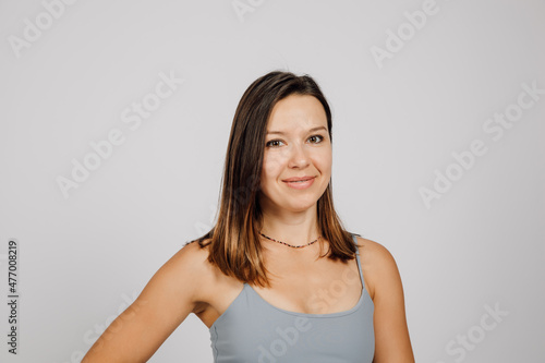 Beautiful brunette posing. Portrait of happy young woman in gray top for yoga or fitness poses on gray isolated background in studio  she is standing sideways.