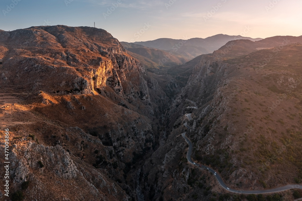 Deep narrow mountain gorge, lit by setting sun with road winding along right side, Crete, Greece