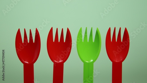 Three red and one green plastic singel use disposable forks close yp on light green background