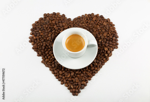 Heart shape made from coffee beans and a cup of cappuccino coffee on a white background. Flat lay. Coffee love concept