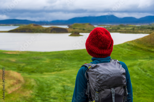 Woman hiker with a red wool hat and a backpack enjoys the view of Skutustadagigar (Skútustaðagígar) a series of pseudocraters formed by lava flow, surrounded by Lake Myvatn wetlands. Iceland