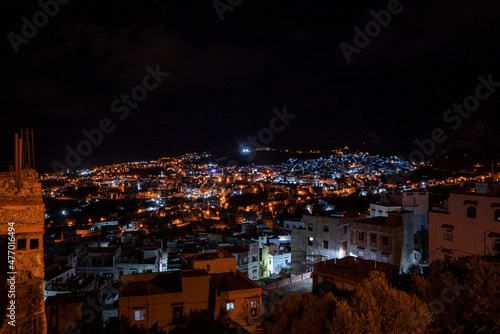 High angle view of lit residential buildings in Chefchaouen old town under the dark night sky © Aerial Film Studio