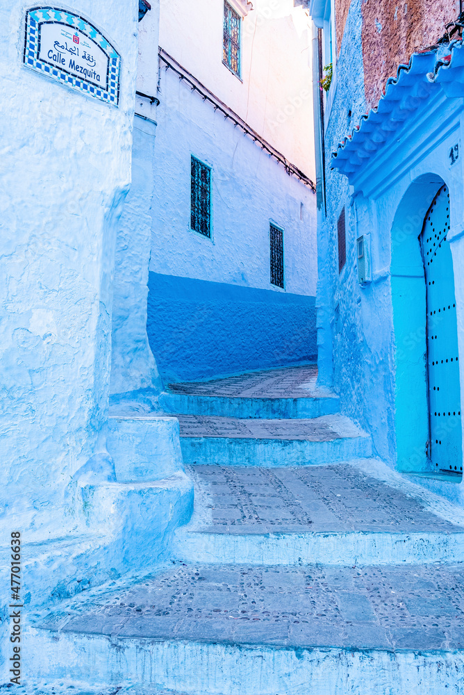 Naklejka premium Chefchaouen, Morocco. October 10, 2021. Traditional residential buildings along narrow street painted in blue and white color