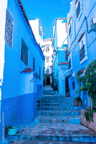 Blue colored residential alley with staircase and potted plants leading to houses on both side, the blue city in the Morocco © Aerial Film Studio
