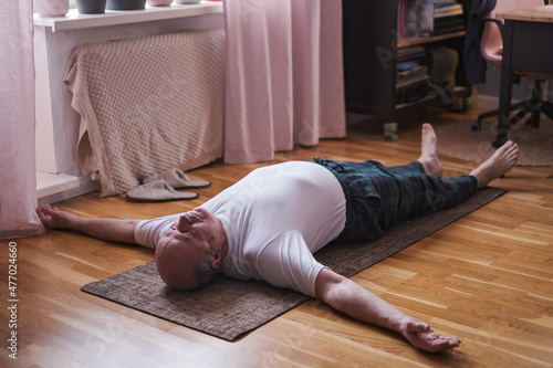 Canvas Senior man meditating on a wooden floor and lying in Shavasana pose