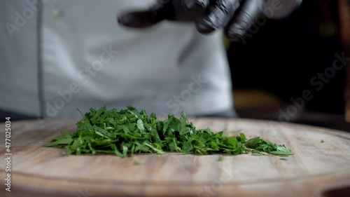 A chef in black gloves chops parsley on wooden cut board