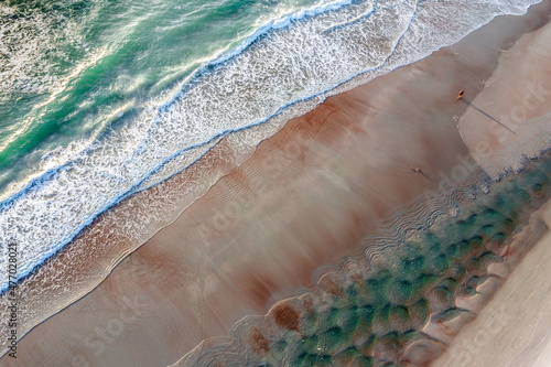 Aerial of Florida beach with a woman walking on wet sand between aqua tide pools and incoming Atlantic ocean.