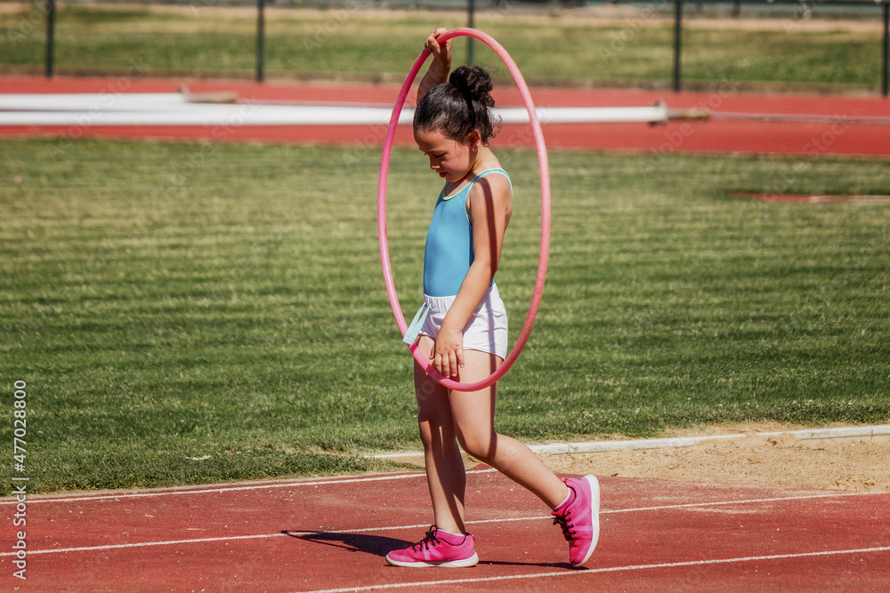 Niña con el aro hula hula como parte de su entrenamiento de atletismo en las instalaciones deportivas. Niña con el aro hula hula como parte de su entrenamiento de atletismo en las instalaciones deportivas.