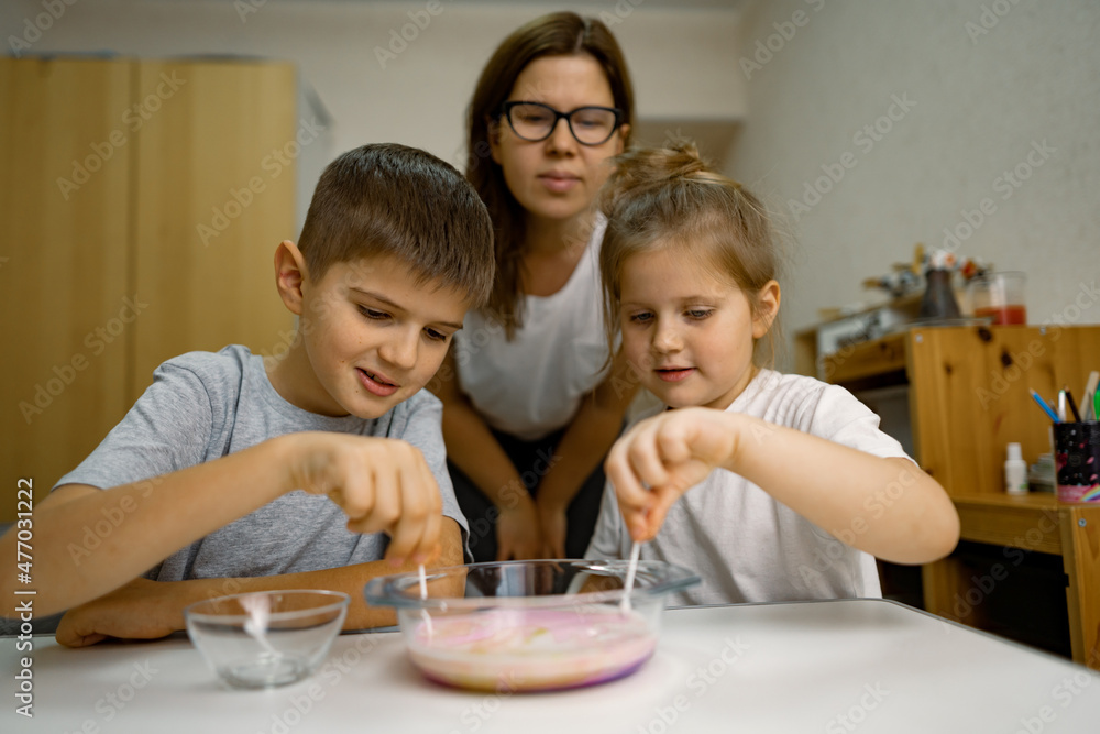 Mom and children are having fun at home, experimenting with milk and paints Mom and children are having fun at home, experimenting with milk and paints