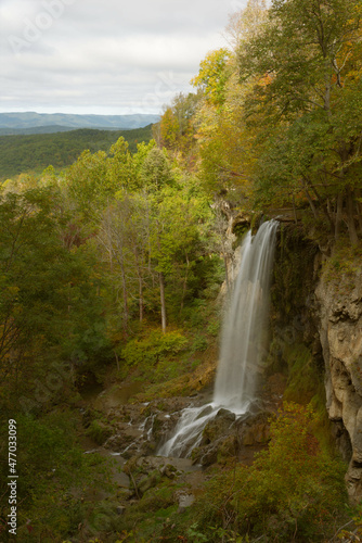 A mountain waterfall cascades over boulders with trees in full autumn seasonal color