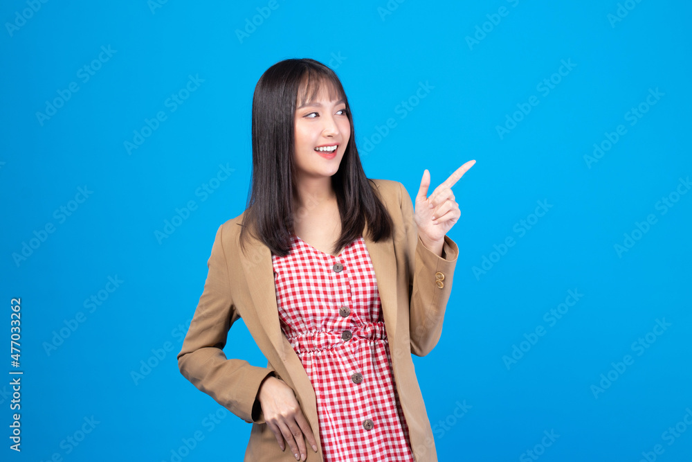Beautiful Asian woman wearing casual clothes smile and pointing finger at copy space isolated on blue background studio portrait. Beautiful Asian woman wearing casual clothes smile and pointing finger at copy space isolated on blue background studio portrait.