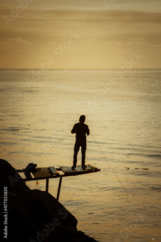 silueta de un hombre pescadno en la costa