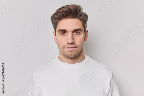 Portrait of handsome brunet unshaven adult man looks with calm confident expression has serious look wears casual jumper poses for making photo against white background being hard to impress © wayhome.studio 