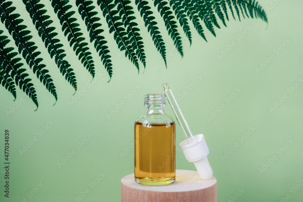 Serum bottle on wooden stand on green background with fern leaf. Natural cosmetics for face, mock up. Close up, copy space Serum bottle on wooden stand on green background with fern leaf. Natural cosmetics for face, mock up. Close up, copy space