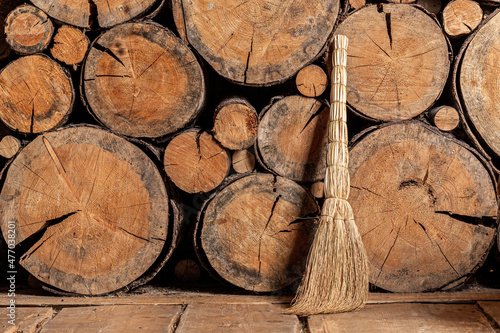 A broom stands against a wall made of sawn trees. Composition in a rustic style