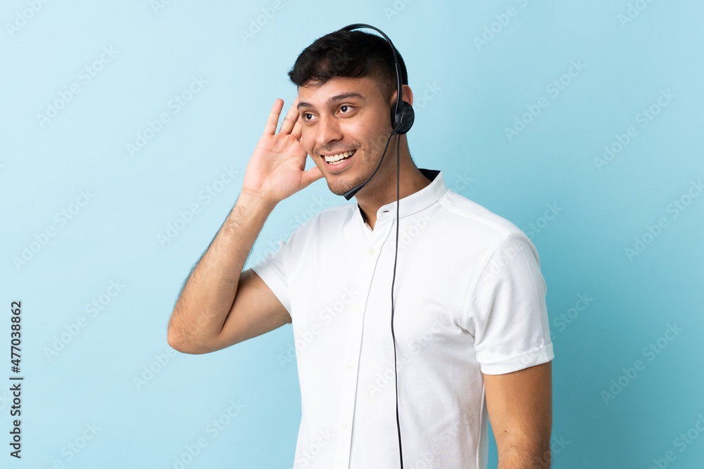 Telemarketer Colombian man working with a headset over isolated background listening to something by putting hand on the ear Telemarketer Colombian man working with a headset over isolated background listening to something by putting hand on the ear