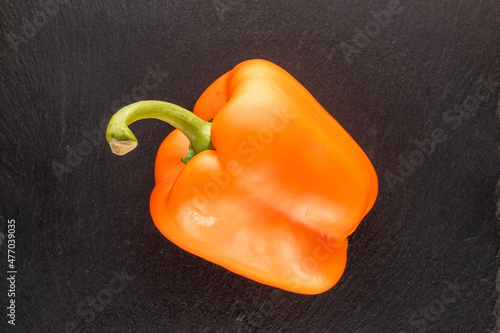 One orange fresh sweet pepper on a slate stone, close-up, top view.